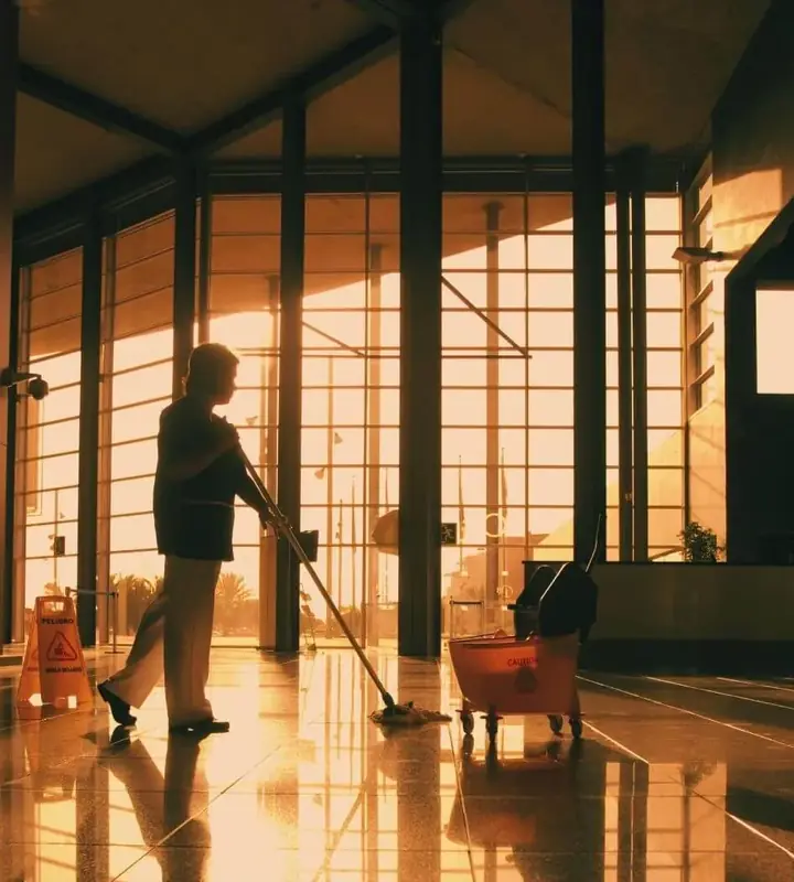 Cleaning professional mopping a polished floor in a large glass-walled commercial building
